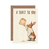 Greeting card with a rabbit holding a piece of toast and 'A Toast to You!' text on a beige background.