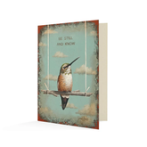Card with a painting of a hummingbird on a stick swing with in front of a sky full of clouds. It reads "Be Still And Know" above the bird.