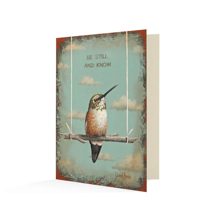 Card with a painting of a hummingbird on a stick swing with in front of a sky full of clouds. It reads "Be Still And Know" above the bird.