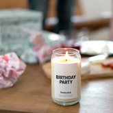 Candle in foreground, with presents and crumpled wrapping paper out of focus in the background.