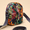 A small crossbody bag with a dark navy blue base and a vibrant multicolor floral print in orange, green, and red. It features a matching dark navy webbed strap and gold-tone hardware, set against a solid beige background.