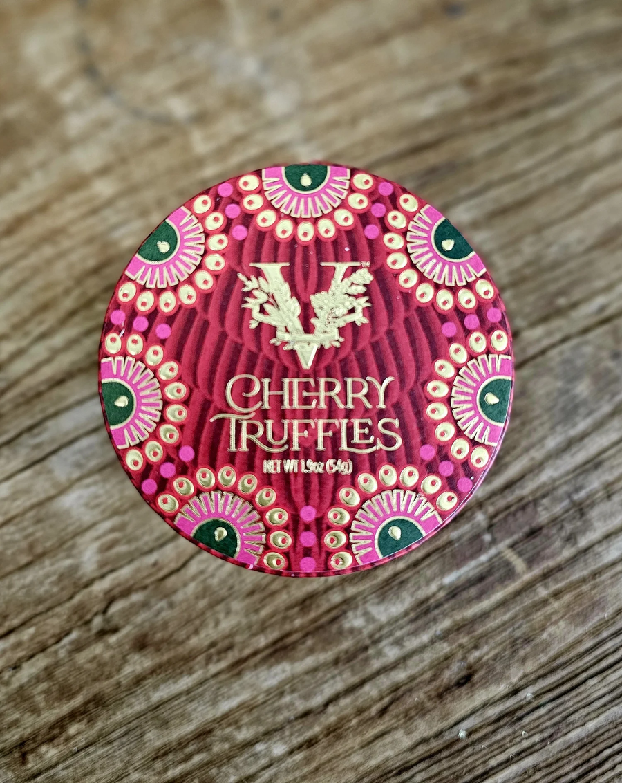 Red round chocolate box with intricate gold, green and pink details, that reads "Cherry Truffles". Set in front of a wood background. 