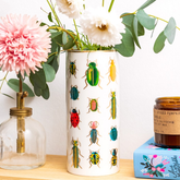Decorative vase with an illustrative bug pattern on a table with flowers and a candle.