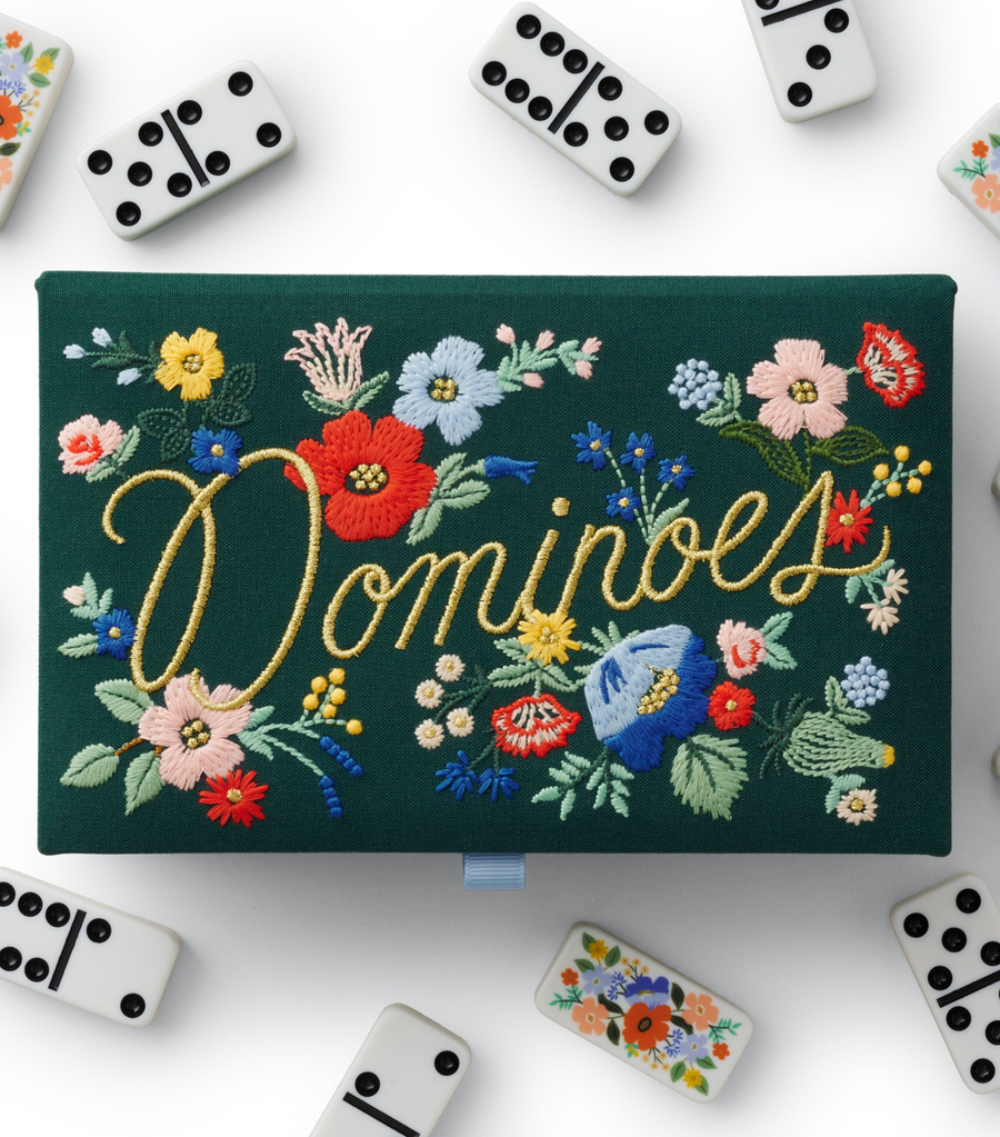 Dark green dominoes box with embroidered flowers, and dominoes scattered around the box. 