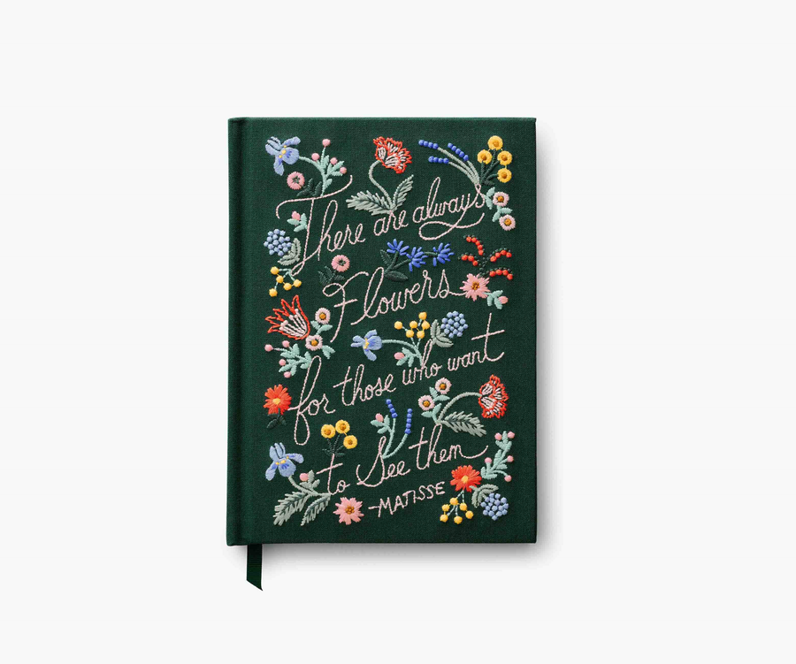 Dark green embroidered notebook with the text "There are always flowers for those who want to see them. -Matisse". Bright colored flowers are embroidered on the journal, laid against a white background.