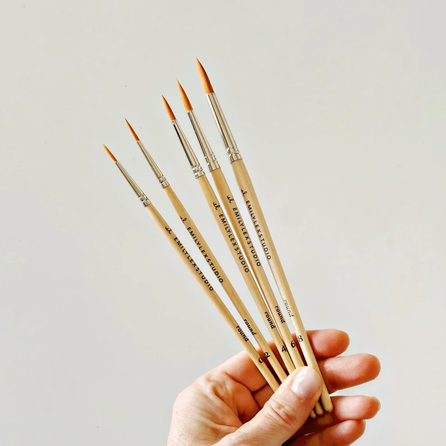 Hand holding a set of paintbrushes against a plain cream. background