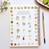 Backside of a watercolor workbook displaying each finished page, with a paintbrush to the right, against a white background. 