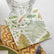 A cocktail napkin with a fern pattern styled on a table setting with a glass, a woven placemat, and a green bowl.
