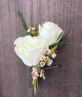 Boutonniere made of white spray roses and wax flower against a grey suit jacket.