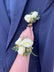 Hand displaying matching corsage and boutonniere in white flowers, against a nay blue suit jacket.