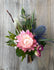 Boutonniere made with pink and blue flowers and greenery.