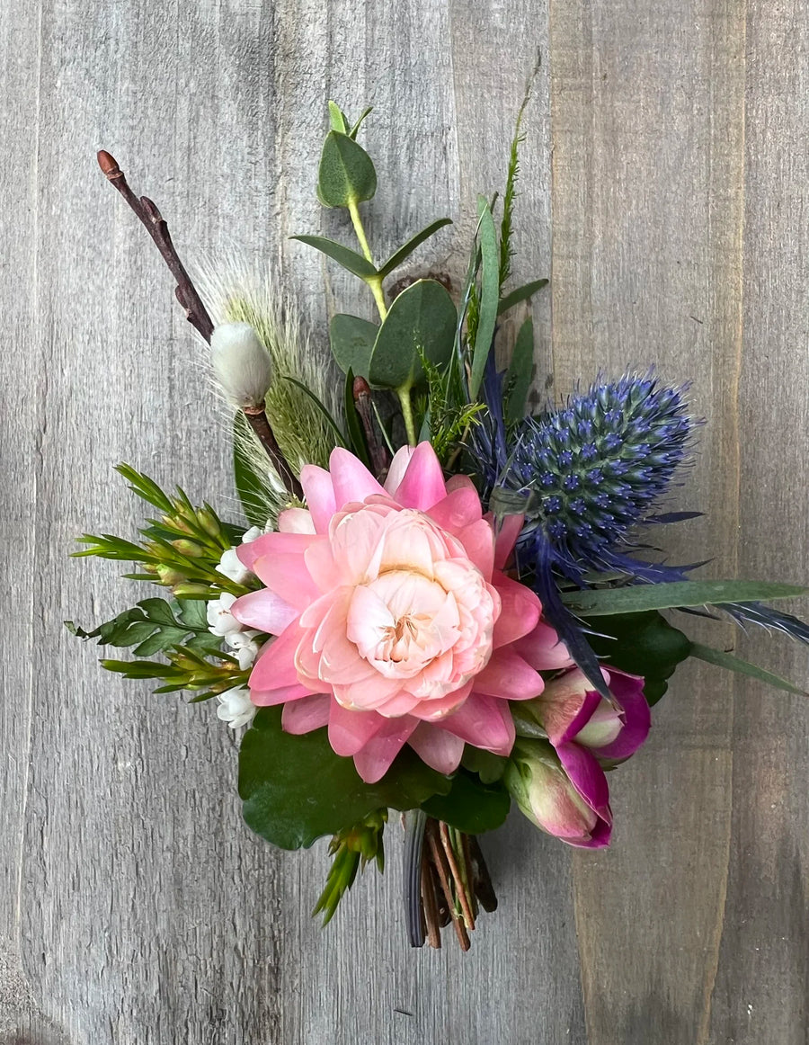 Boutonniere made with pink and blue flowers and greenery.