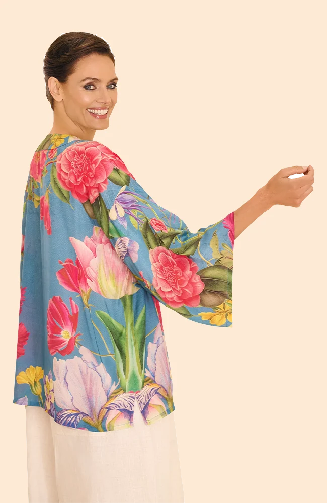 A woman wearing a denim-blue kimono with a large-print floral pattern in vibrant pinks, purplesm and a small amount of yellow, set against a light background.