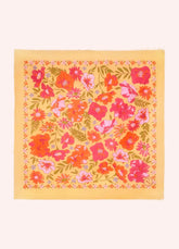 A square scarf with a vibrant floral pattern, featuring orange, pink, and red flowers with green leaves on a pale yellow background, laid flat against a light cream backdrop.