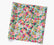A square sheet of wrapping paper featuring a colorful, dense floral print on a light blue background, shown at an angle against a plain white background.