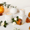 Two white candles surrounded by gardenia flowers and amber pieces on a white table.