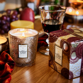 Candle, candle box, and wine goblet on table with decadent elements out of focus in the background.