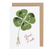 White card with watercolor painting of a small woman holding an oversized four leaf clover. Cursive red text below reads "Good Luck". 