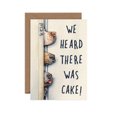 Greeting card with dogs peeking around a door and text "We heard there was cake!" on a white background.
