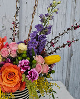 Three quarter shot of a brightly colored arrangement in a vase with a black and white striped ribbon. 