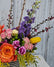 Three quarter shot of a brightly colored arrangement in a vase with a black and white striped ribbon. 