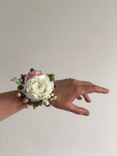 Hand displaying a corsage made in white and pink flowers.
