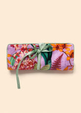 Rolled-up lavender jewelry roll with a vibrant floral and botanical pattern in purple, pink, green, and orange, tied with a sage green ribbon. 