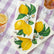 Napkins with lemon design on a purple checkered tablecloth with glasses of tea.