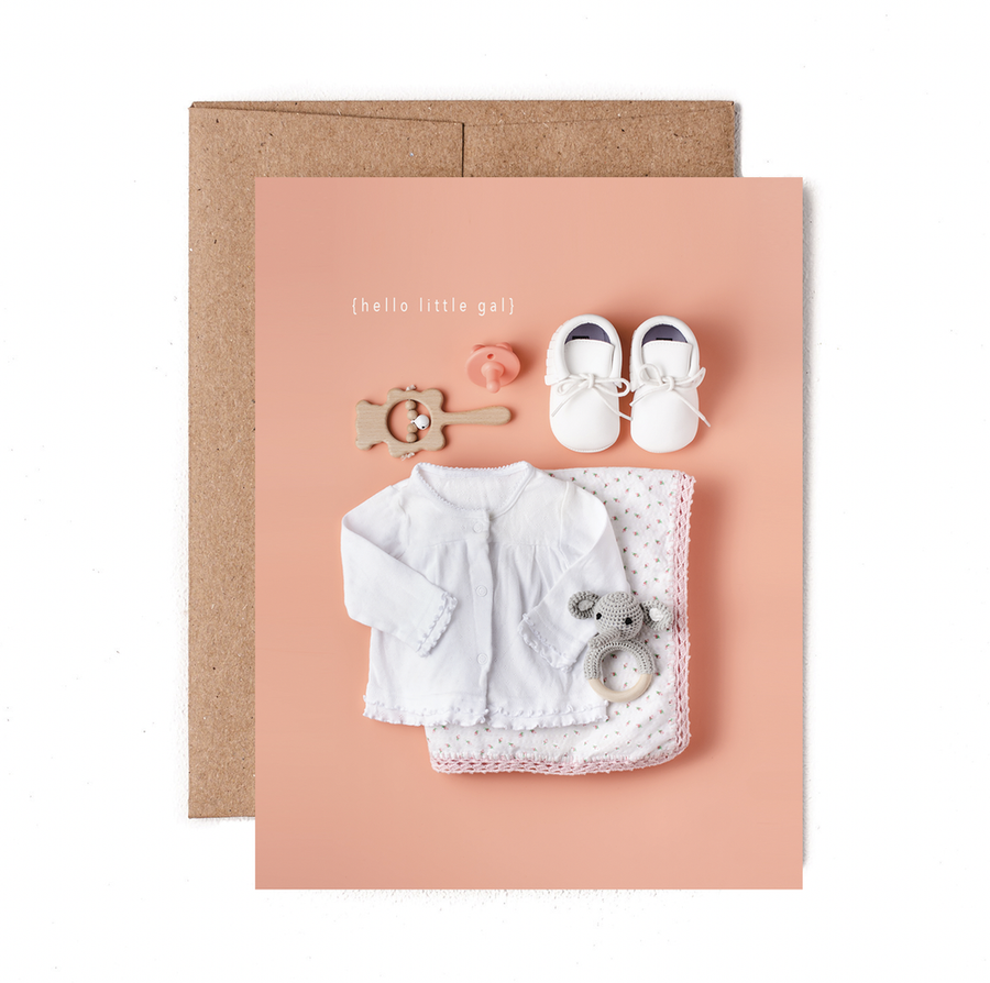 Pink greeting card with baby clothes and toys, with the words "Hello little gal".