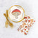 White cocktail napkins printed with red and brown mushrooms, arranged on a white marble surface with gold forks and a gold-rimmed plate.
