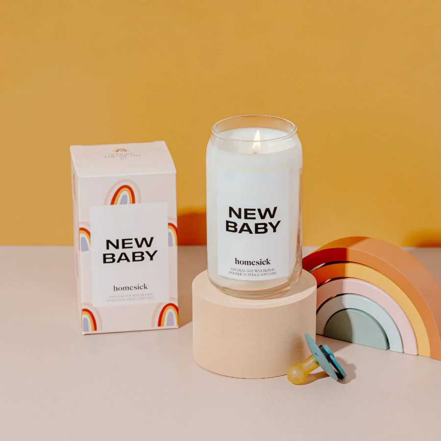 Candle and candle box sit next to a rainbow baby toy and pacifier, in front of a sunflower yellow background. 
