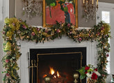 A white mantle and fireplace, decorated with a holiday garland. Green ribbon, pink, gold, and silver ornaments, and yellow lights adorn the garland, which sits below a painting with two candelabras on either side. 