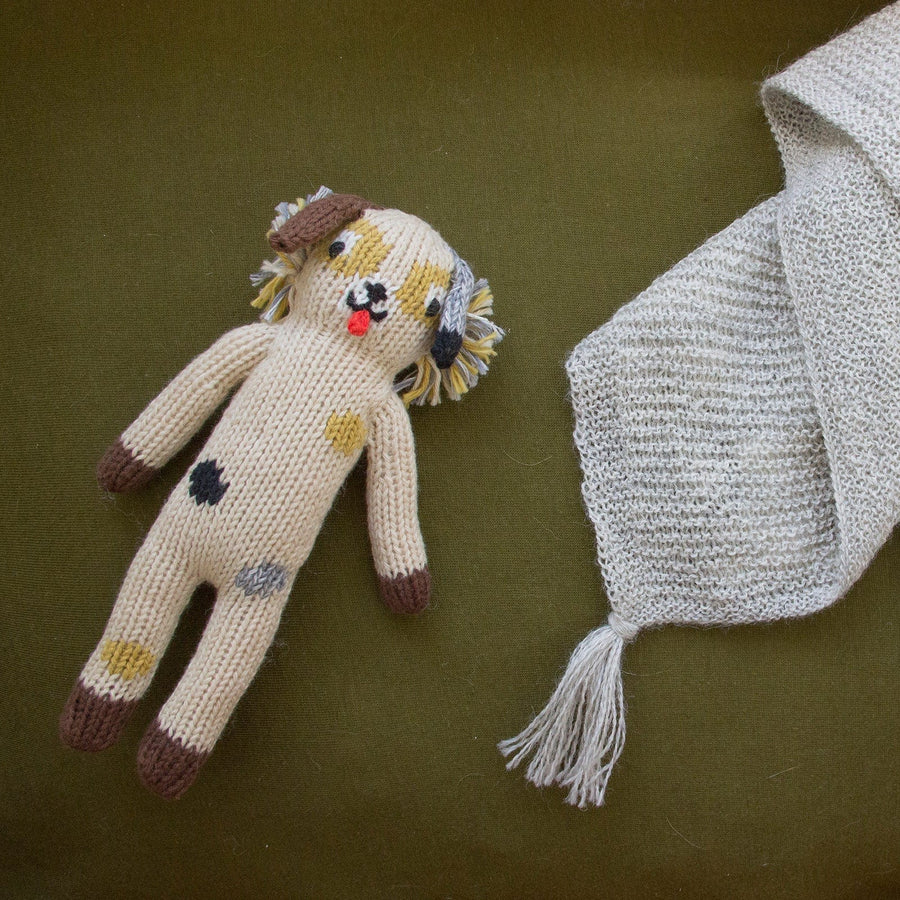 Hand-knit dog rattle in shades of brown, grey, black and yellow, on a green background.