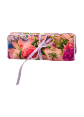 Rolled up pink jewelry roll with a floral pattern in pink, purple and reens, tied with a lavender ribbon.