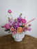 Floral arrangement in pink, purple and peach hues set in a neutral ceramic pot. 