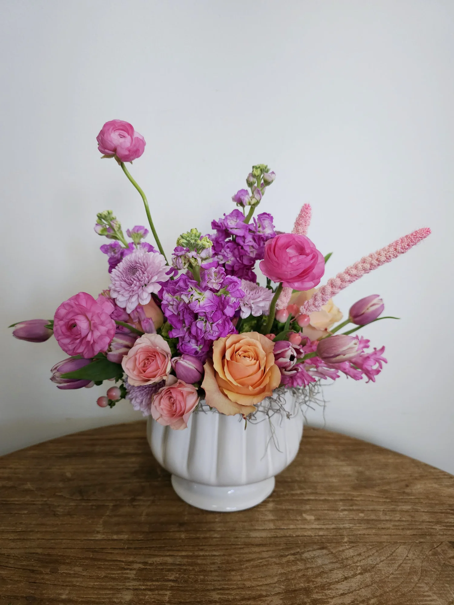 Floral arrangement in pink, purple and peach hues set in a neutral ceramic pot. 