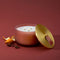 A three-wick candle in a ribbed terracotta glass jar with a gold-toned lid leaning beside it, styled on a dark red background with orange peel and star anise.