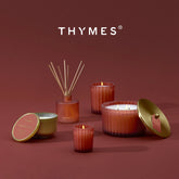 A set of THYMES reed diffusers and candles in a coordinated terracotta and gold colorway, arranged on a matching terracotta background with the brand name displayed at the top.