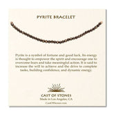 A cream, Cast of Stones branded backing card holds a crystal-beaded bracelet labelled "Pyrite Bracelet". There is an informational paragraph below the bracelet detailing the properties of the crystal and its benefits.