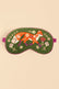 A green embroidered sleep mask featuring a whimsical orange fox, white flowers, and purple botanical details, shown against a solid beige background.