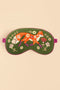 A green embroidered sleep mask featuring a whimsical orange fox, white flowers, and purple botanical details, shown against a solid beige background.
