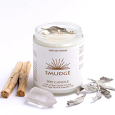 White candle behind a smudge stick, clear quartz, and sage leaves lying in front of a white background.