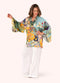 Woman wearing a colorful floral kimono with white pants on a light background.
