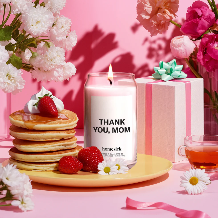 Candle surrounded by pancakes, strawberries, presents, and flowers. 
