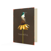 A black card with a hummingbird atop a yellow coneflower. The text below says "Thankful".