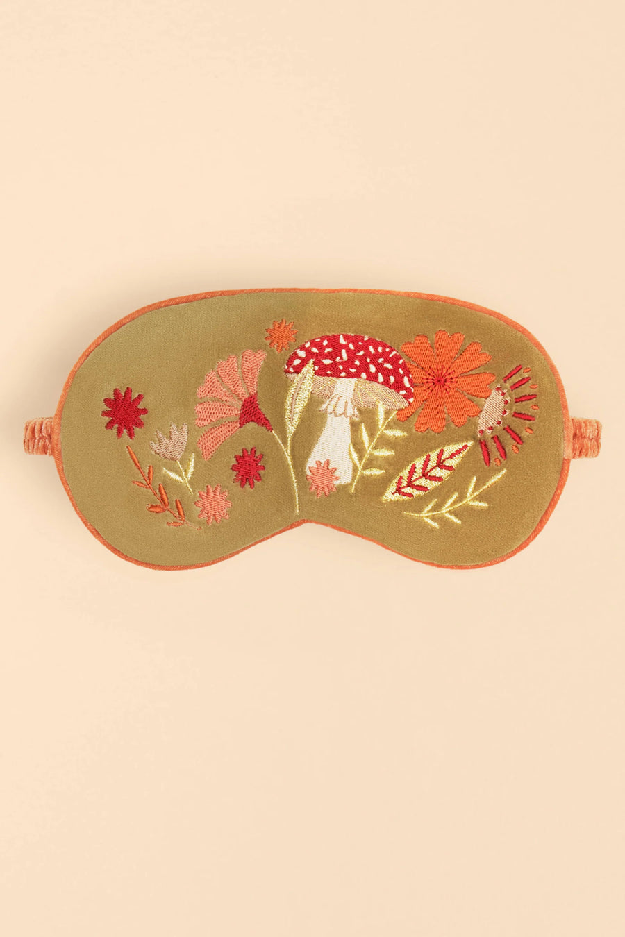 An olive-green embroidered sleep mask with orange trim and detailed floral and mushroom embroidery in red, pink, orange, and white, set against a solid beige background.
