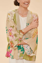 Woman wearing a cream kimono with a large-print tropical floral pattern, against a beige background