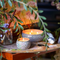 Two tin candles sitting atop an easel with paintbrushes, paint tubes, and a canvas our of focus in the frame.