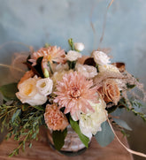 Floral arrangement in a neutral pink and white color palette with whispy greens and accent, in a vase wrapped in a burlap inspired ribbon.