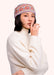 Woman in a cream colored sweater wearing a headband with a geometric orange, purple and gold pattern on it, against a light background.